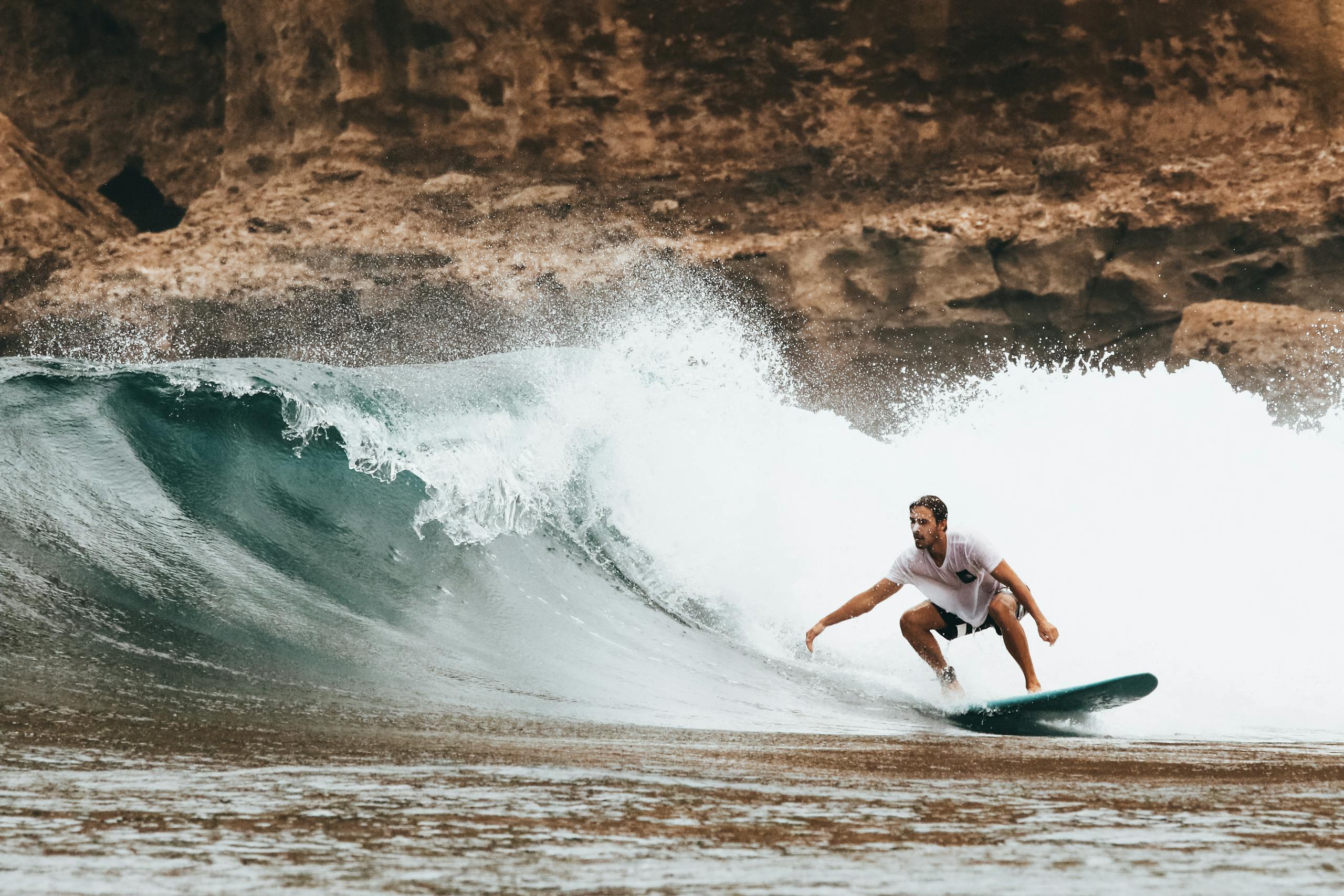 Surfer rides a powerful wave near a rocky coast, capturing the thrill of summer ocean sports.